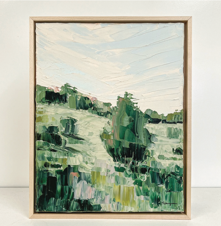 Framed abstract landscape painting with green and blue tones on a white wall.