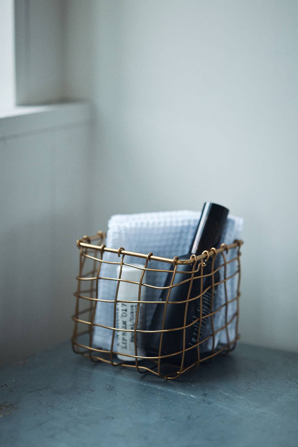 Wire basket with books on a light blue surface against a white wall