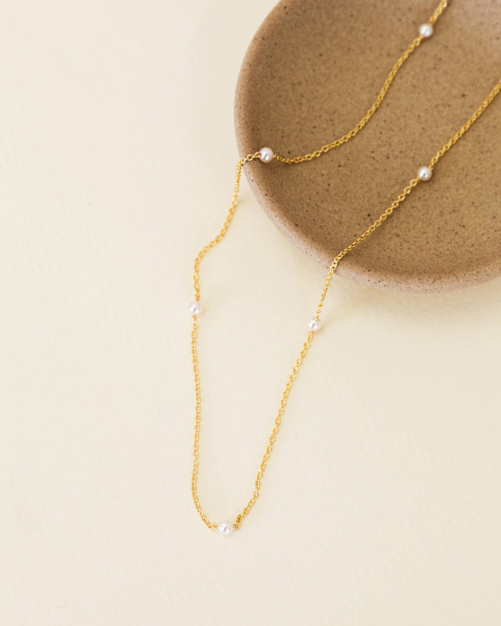Gold necklace with small pearls on a beige surface