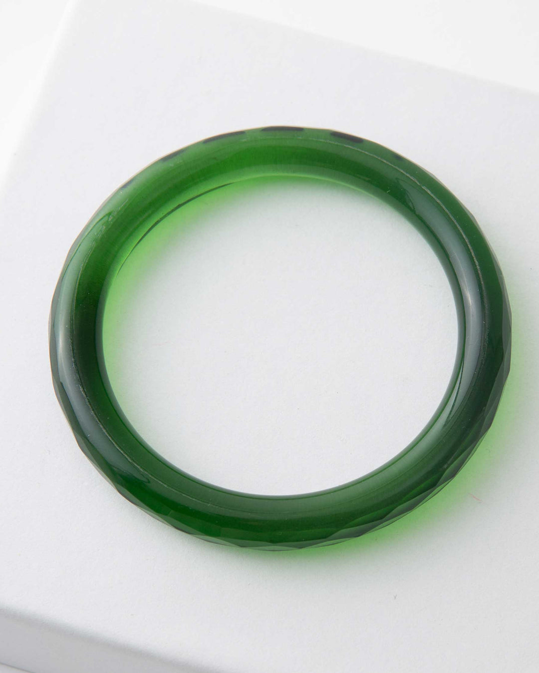 A single green glass bangle bracelet displayed on a white surface.