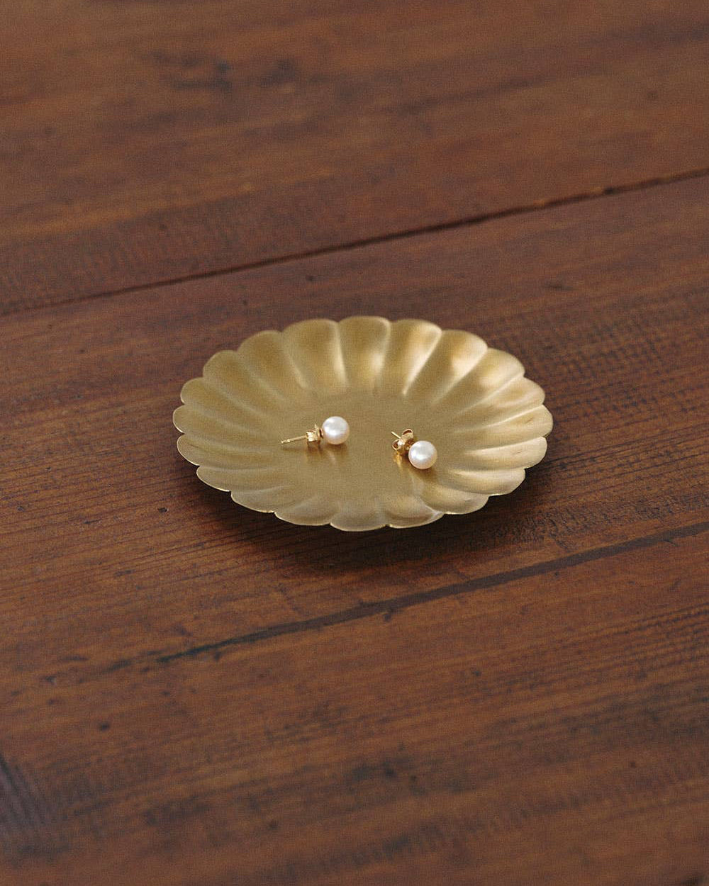 Gold earring on a matching gold dish on a wooden surface