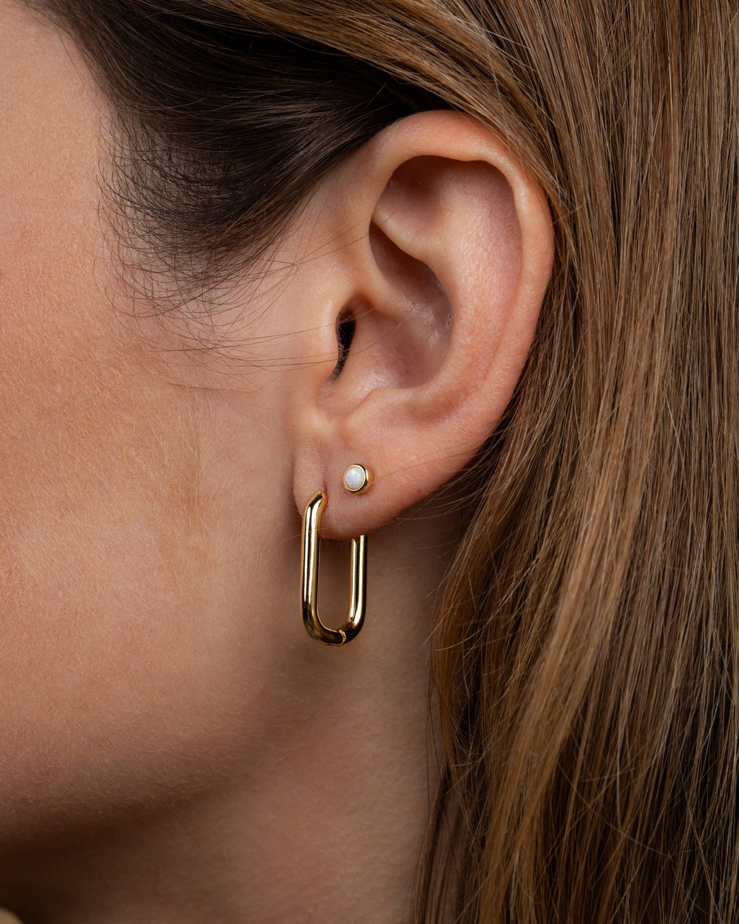 Close-up of a person wearing a gold hoop earring with a pearl accent.