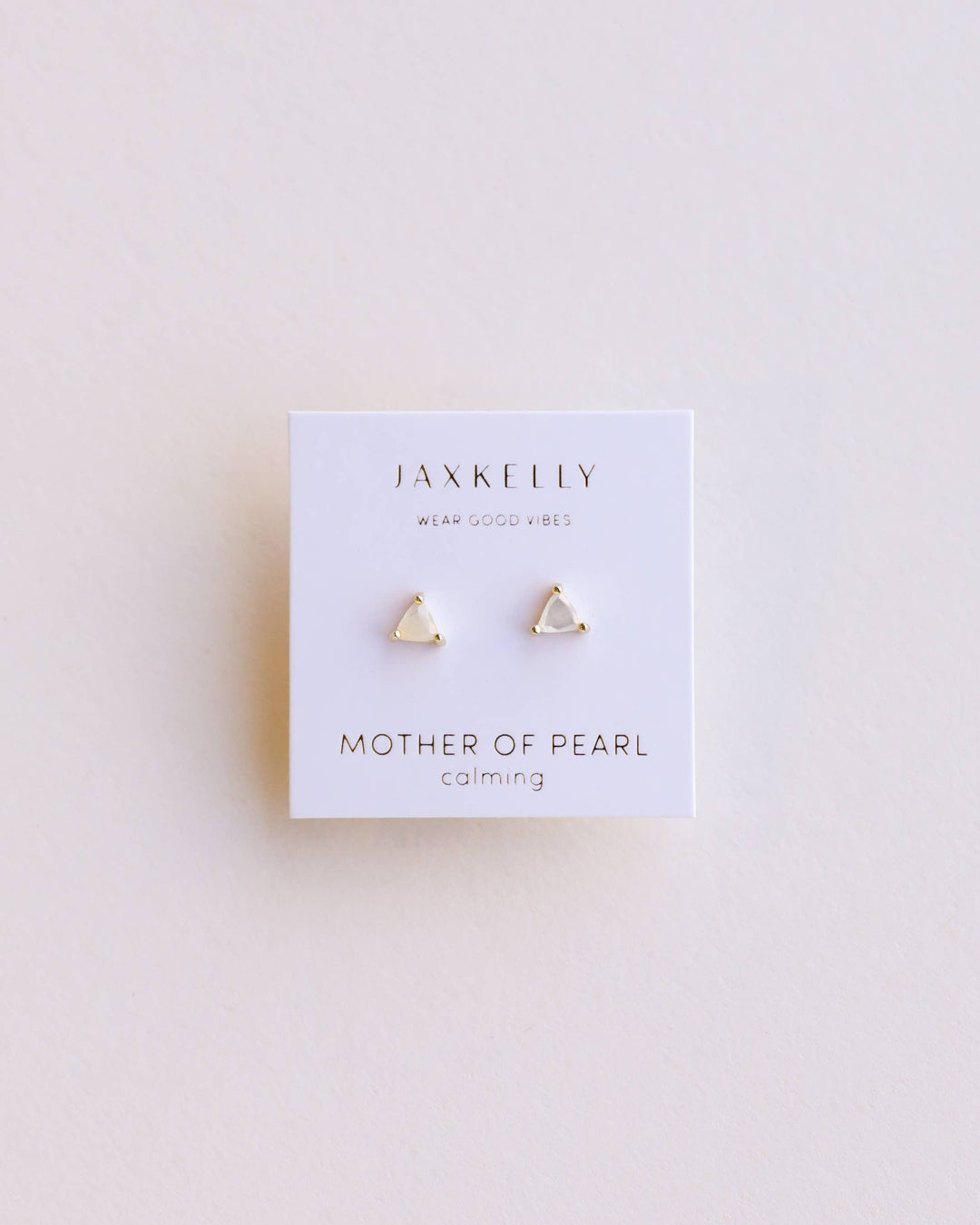 Pair of gold triangular earrings on a Jax Kelley branded card with 'Mother of Pearl' and 'Calming' text on a light background.
