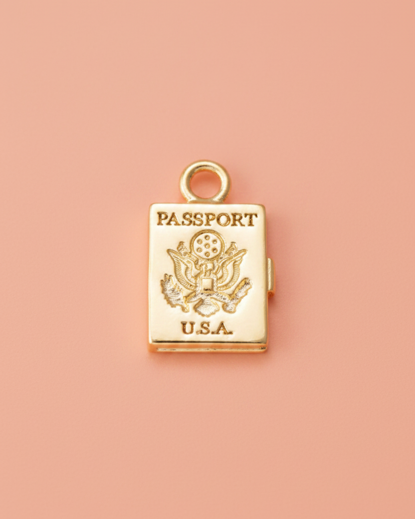 Gold passport-shaped charm on a light coral background