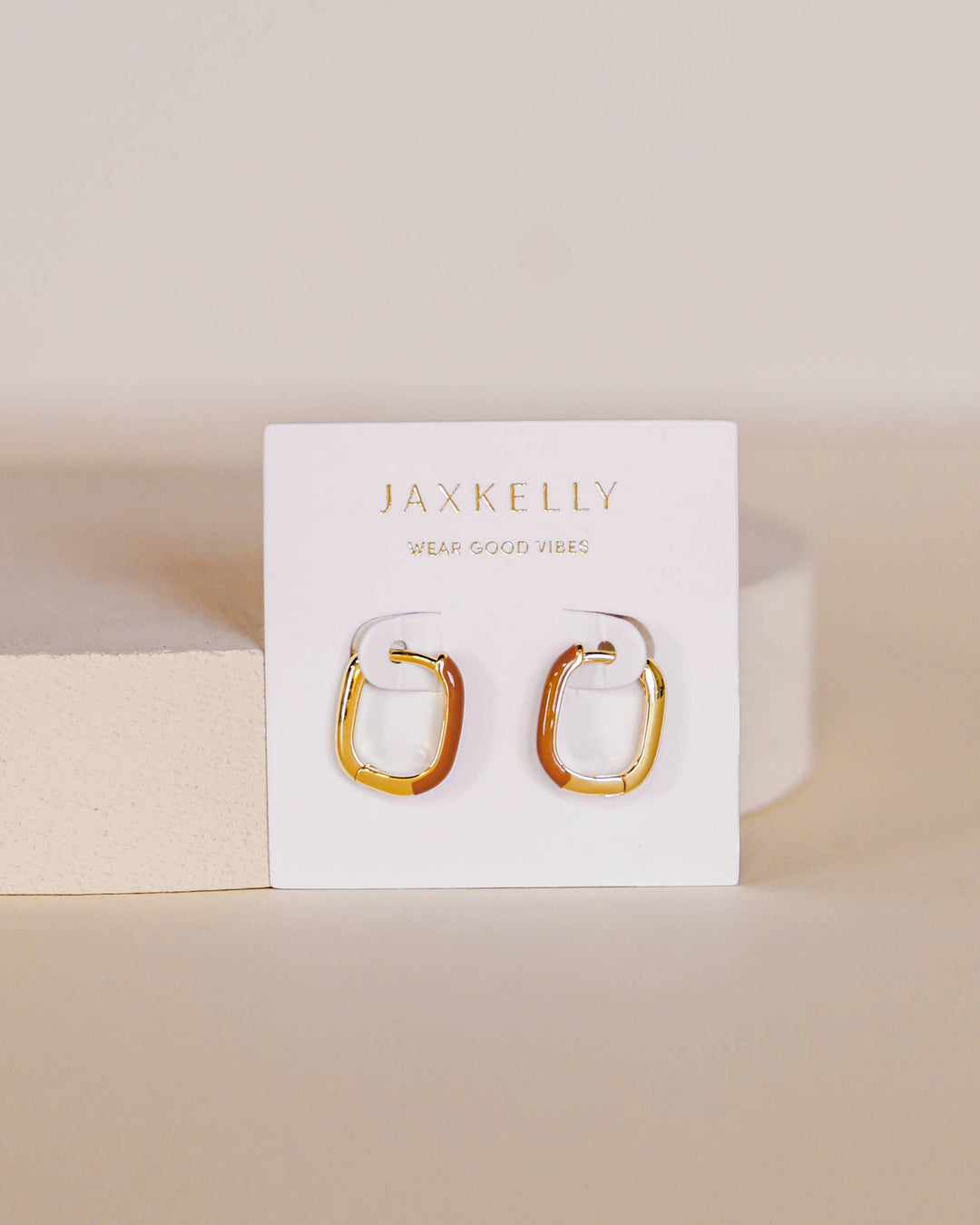 Gold hoop earrings on a Jax Kelley branded card with a beige background
