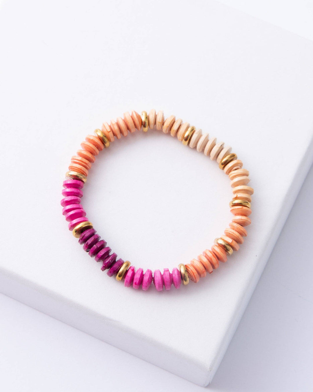 A stretchy bracelet with dainty paper bead discs in shades of pink, orange, and yellow, displayed on a white surface.