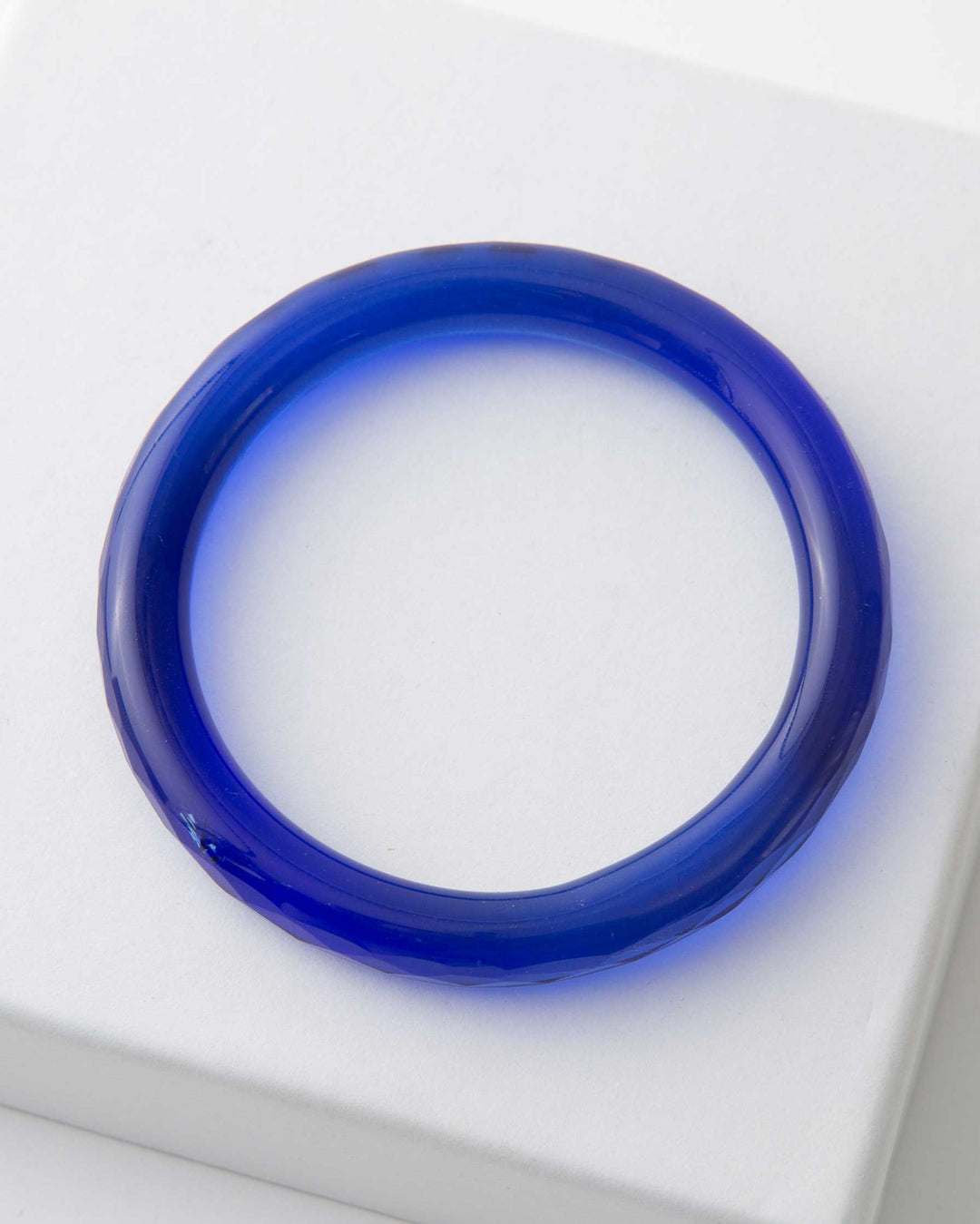 A single cobalt blue glass bangle presented on a white surface.