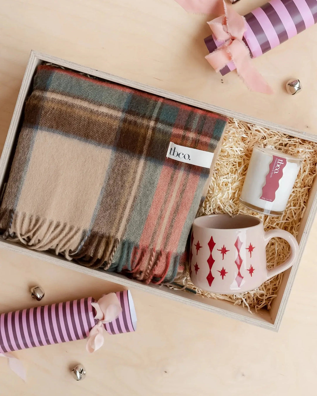 Gift set with plaid scarf, mug, and striped ribbons in a box on a beige background
