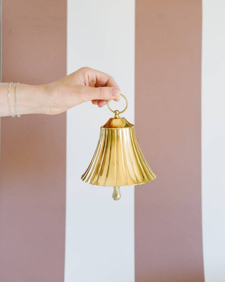 Hand holding a gold bell against a striped background