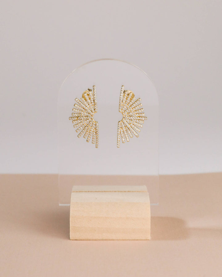 Gold earrings on a white stand with a beige background