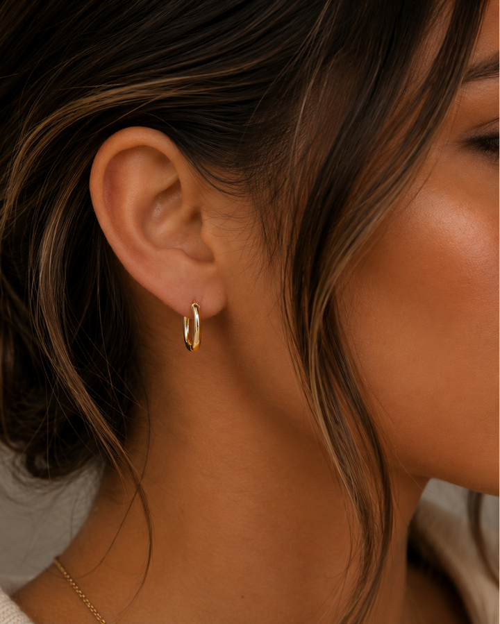 Close-up of a person wearing a gold hoop earring with a neutral background
