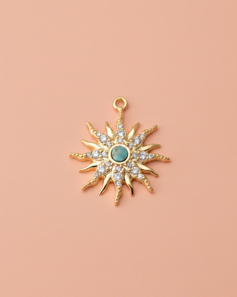 Gold sunburst star charm with a central round turquoise stone and clear rhinestone accents, displayed on a light coral background.