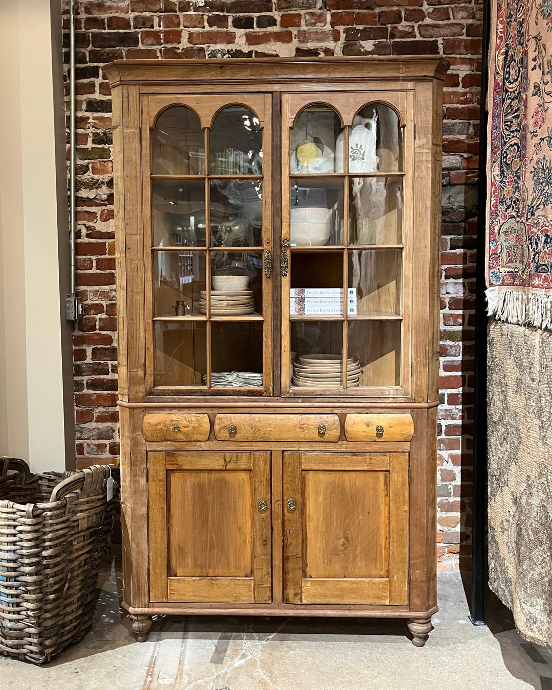 Wooden cabinet with glass panels against a brick wall.