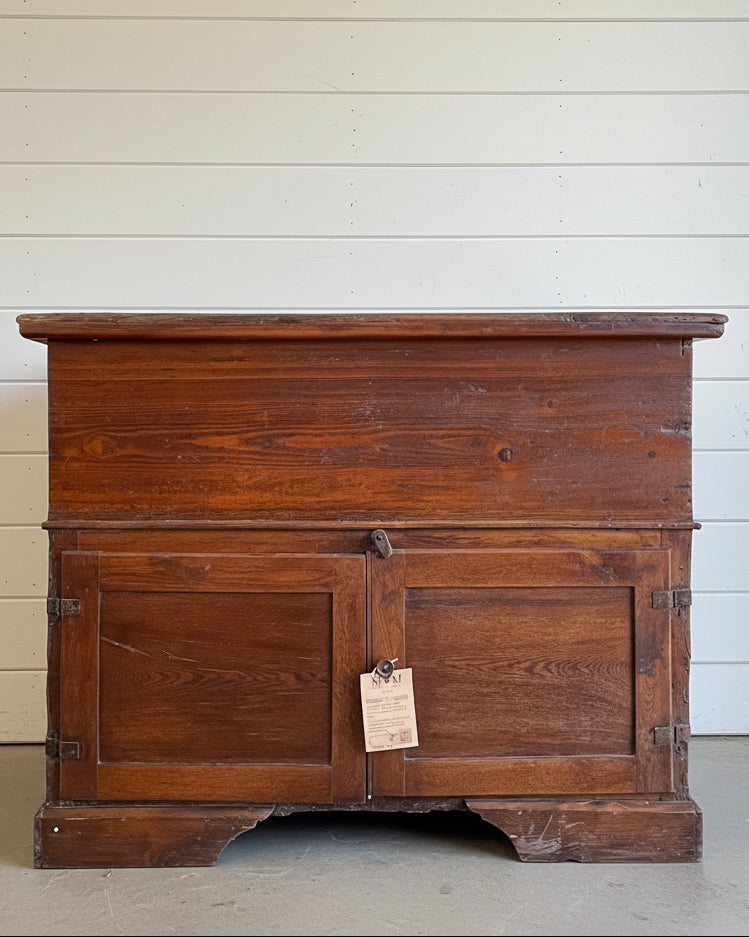 Vintage wooden chest with a tag on a concrete floor against a white wooden wall.