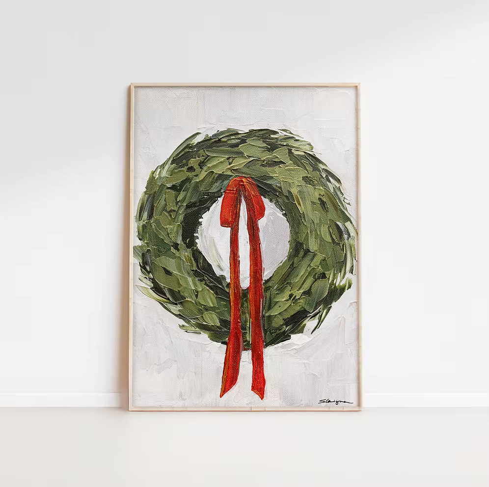 Framed artwork of a green wreath with a red ribbon on a white background
