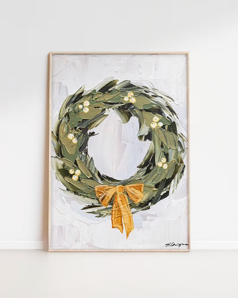 Framed artwork of a green wreath with a gold bow on a white background