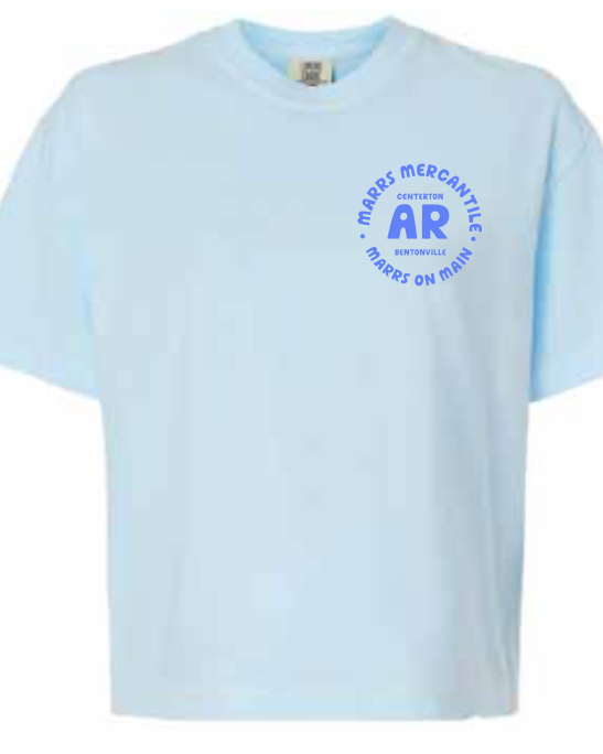 A light blue short-sleeve crewneck t-shirt with a blue circular graphic on the left chest featuring the text 'MARRS MERCANTILE CENTERTON AR BENTONVILLE MARRS ON MAIN