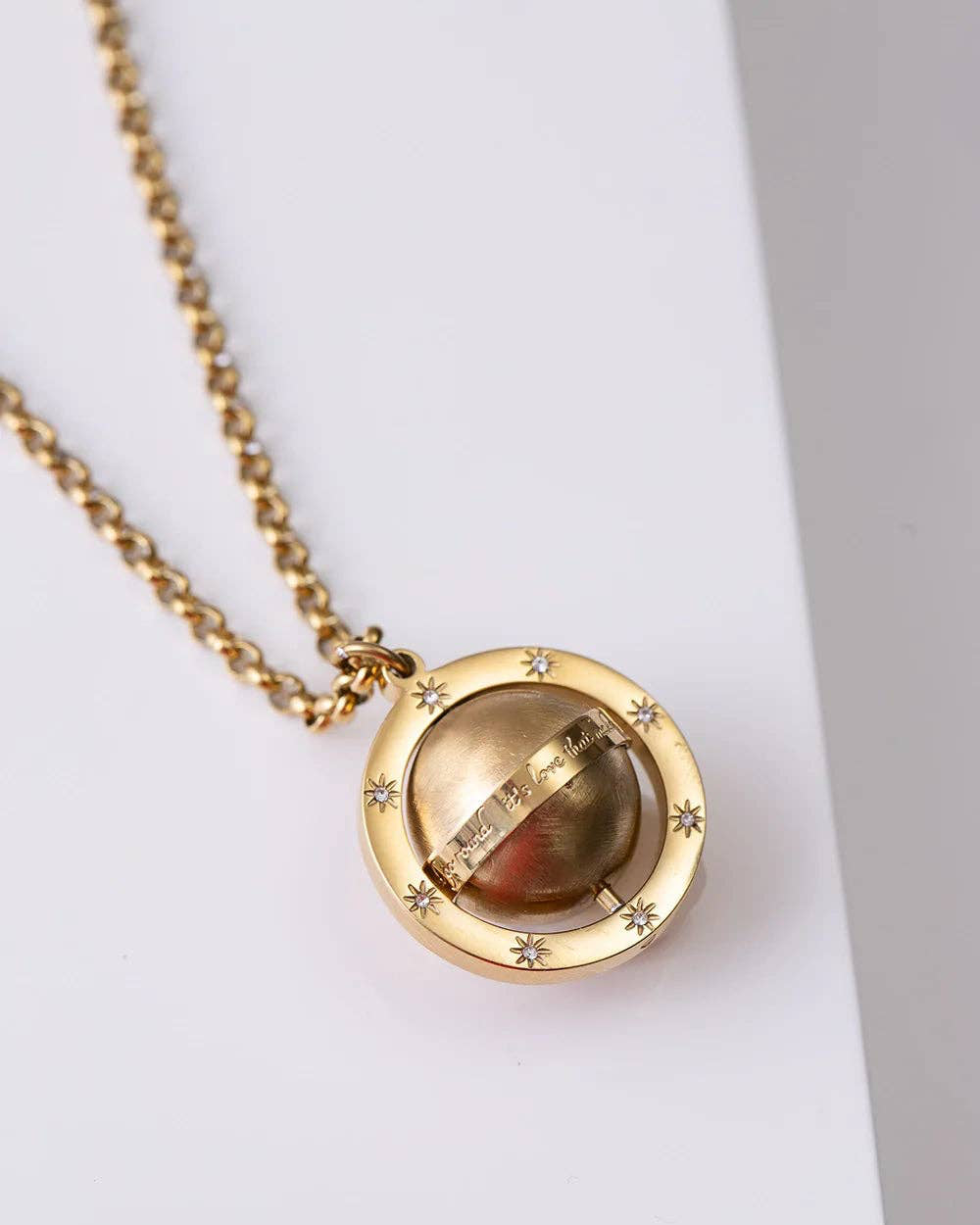 Gold necklace with a circular pendant on a light purple surface