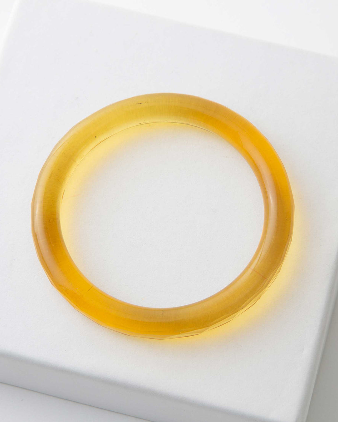 A single yellow glass bangle presented on a white surface.