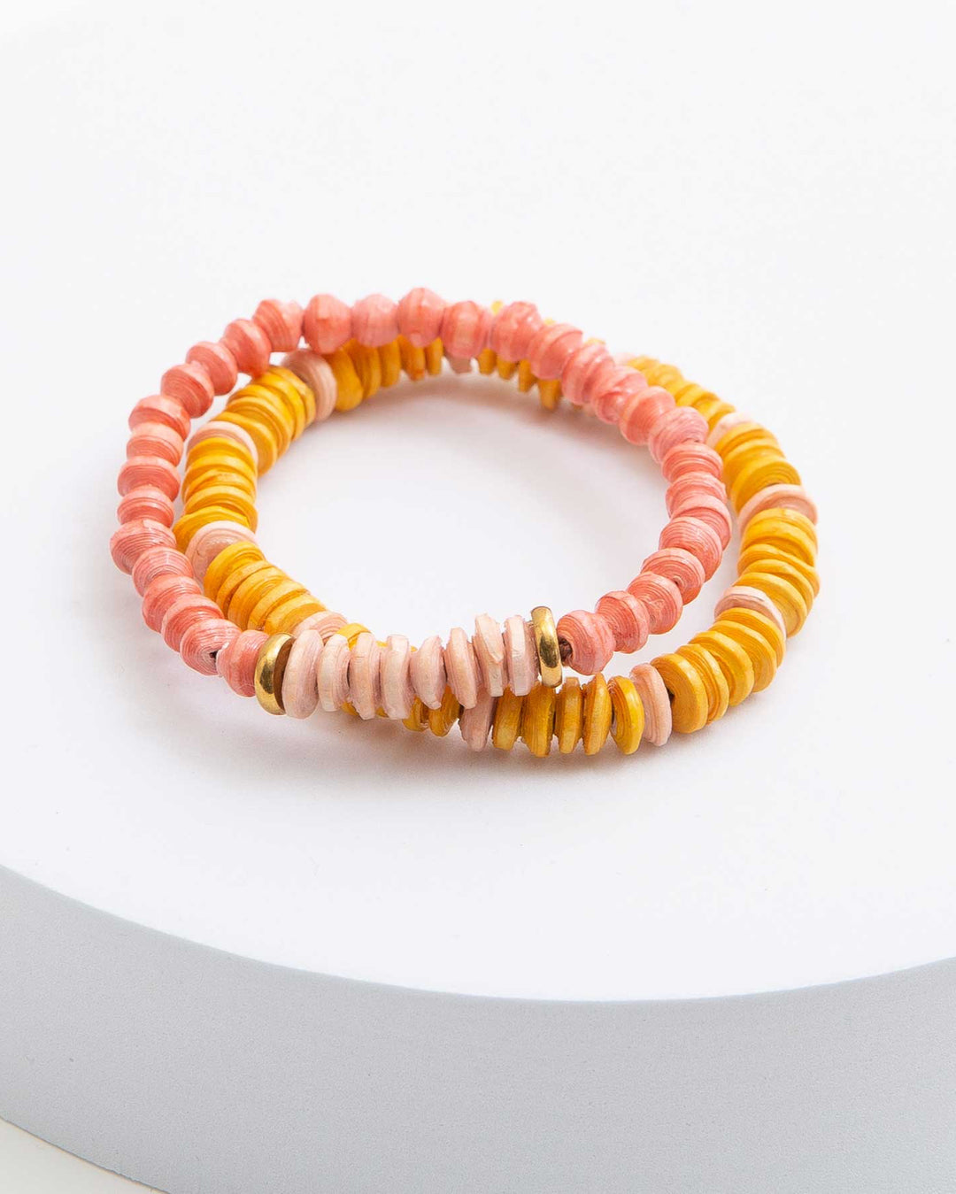 Two bracelets with pink, orange, and yellow paper beads, accented with brass beads on a white surface.