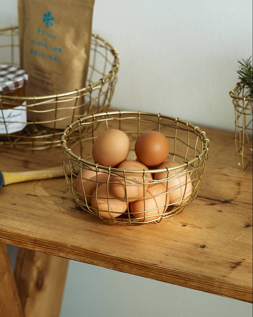 Gold wire baskets with eggs and a package on a wooden surface
