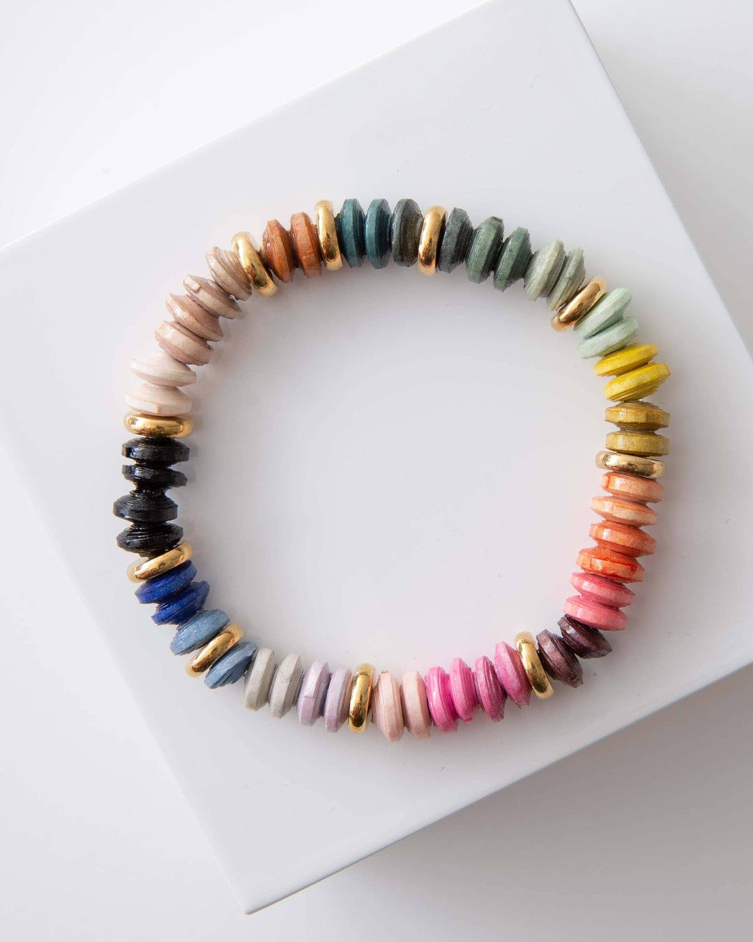 A stretchy bracelet made of multi-colored paper bead discs, displayed on a white surface.